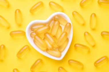 D vitamini ve Omega 3 balık yağı kapsülleri sarı arka planda kalp şeklinde bir tabakta. Sağlık hizmetleri kavramı. Üst görünüm