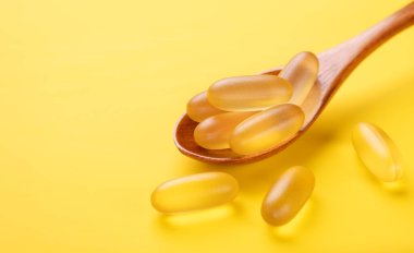 Sarı arka planda Omega 3 haplı tahta kaşık. D vitamini kapsülleri. Kapat.