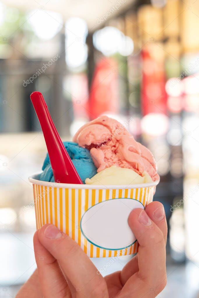 Hand holding paper cup with ice cream on blurred backgruond Travel concept Snack on the street Life style Vertical photo