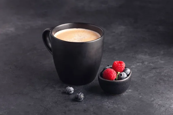 Kaffeebecher auf dunklem Steinhintergrund mit frischen Beeren — Stockfoto