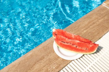 Yüzme havuzunun sınırında taze karpuz. Sıcak yaz seyahati, tatil ve tatil konsepti. Üst Manzara. Uzayı kopyala - Resim