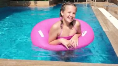 Turkuaz suyla yüzme havuzunda dinlenen mutlu güzel kız. Pembe şişme yüzük üzerinde yüzen kız. Seyahat ve tatil kavramı