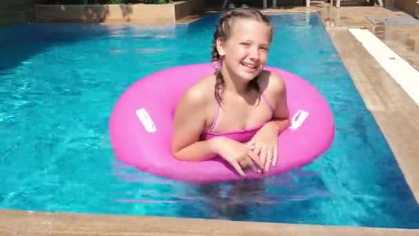 Glückliche schöne Mädchen entspannen im Schwimmbad mit türkisfarbenem Wasser. Mädchen, das auf einem rosa aufblasbaren Ring schwimmt. Reise- und Urlaubskonzept — Stockvideo