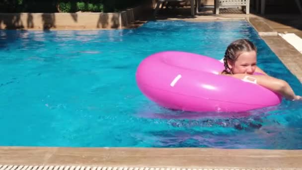Teen girl playing with pink inflatable ring in swimming pool. Girl splashing water. Slow motion