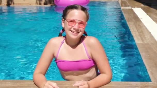 Chica adolescente sonriente en gafas de sol de color rosa en la piscina. Chica quitándose las gafas y buceando bajo el agua — Vídeos de Stock