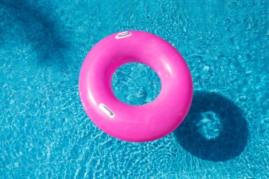 Mavi yüzme havuzunda pembe yüzüklü donut. Üst Manzara. Sıcak güneşli tatil konsepti