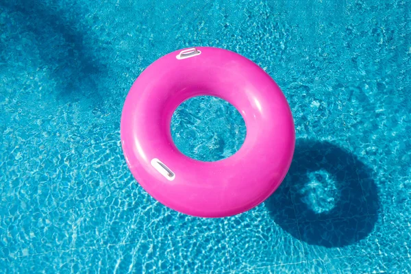 Summer background with pink inflatable ring donut in blue swimming pool. Top view. Hot sunny vacation concept