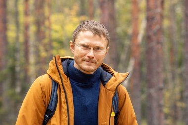 Beyaz bir adam ormanda sırt çantası takıyor. Sırt çantalı bir adam sonbahar ormanında yürüyor.