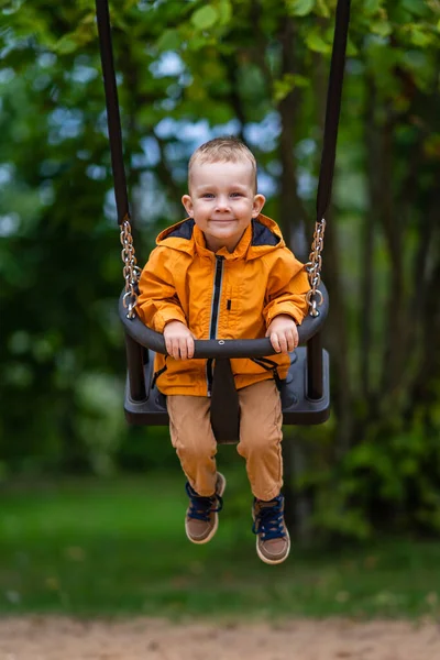 Young Boy Wearing Orange Raincoat Smiles Swings Park — Stock Photo, Image