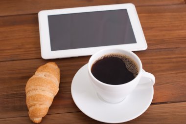 Fincan kahve ve kruvasan dijital tablet masada.