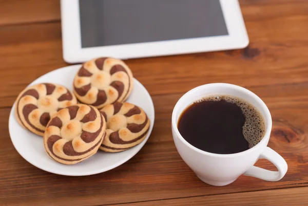 Copa de café y galletas una tableta digital sobre la mesa . — Foto de Stock