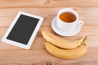 Dijital tablet fincan çay ve bir ahşap masa üzerinde muz.