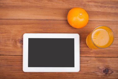 Tablet bilgisayar portakal ve bir bardak meyve suyu ahşap bir masa üzerinde.