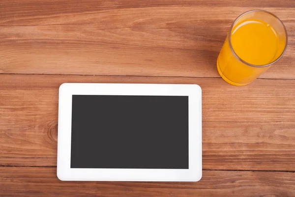 Comprimido digital e um copo de suco de laranja em uma mesa de madeira . — Fotografia de Stock