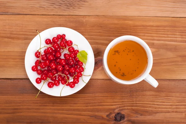 Cup of tea and currants on a wooden table. — Stock Photo, Image