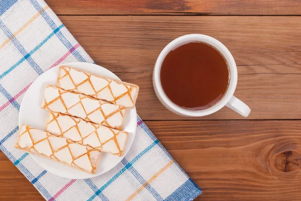 Xícara de biscoitos de chá em uma placa e toalha de mesa em uma mesa de madeira . — Fotografia de Stock