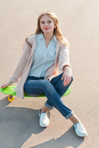Young girl sitting on a skateboard in the street. — Stock Photo, Image