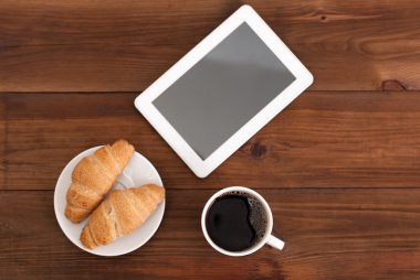 Kahve dijital tablet ve kruvasan ahşap bir masa üzerinde.