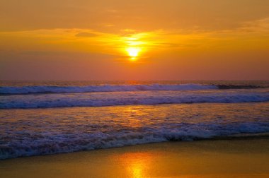 Denizin ya da okyanusun üzerinde güzel bir gün batımı. Canlı ve yumuşak renkler, sihirli ışık. Gökyüzündeki küçük bulutlar, sudaki güneşin yansıması ve kumsaldaki kum. Tropikal bölgelerde romantik zaman kavramı.