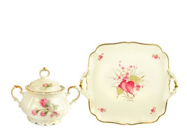 Antika bir porselen kasesi ve her ikisi de pembe çiçek motifleri ve narin altın kaplamalı kare servis tabağı saf beyaz bir zemin üzerinde izole edilir. Bu stüdyo çekimi klasik çay setinin zarif işçiliğini ve klasik güzelliğini vurguluyor.