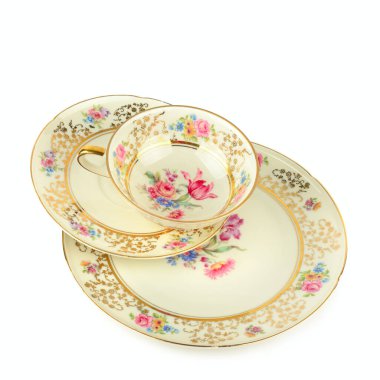 Süslü altın tomarlar ve kremalı arka planda narin çiçek desenleriyle süslenmiş bir fincan, fincan, çay tabağı ve tatlı tabağı içeren zarif bir porselen yığını. Beyaz üzerine bolca fotokopi alanı ile çekim yapmak klasik lüksü çağrıştırıyor. 