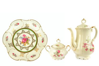 Kahve demliği, şeker kasesi ve dekoratif bir tabak da dahil olmak üzere çok güzel antika porselen parçalar, el boyaması çiçek motifleri ve zengin altın aksanlar içeriyor. Beyaz bir arkaplanda izole edilmiş bu zarif koleksiyon geleneği çağrıştırıyor.