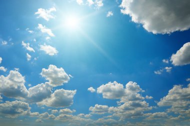 Uçsuz bucaksız mavi gökyüzünde pofuduk beyaz bulutların arasından parlayan güneşin canlı bir görüntüsü. Doğa geçmişi, hava raporları veya geniş kopya alanı olan manevi kavramlar için idealdir.