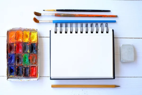 Blocco note, pennelli e vernice sul tavolo — Foto Stock