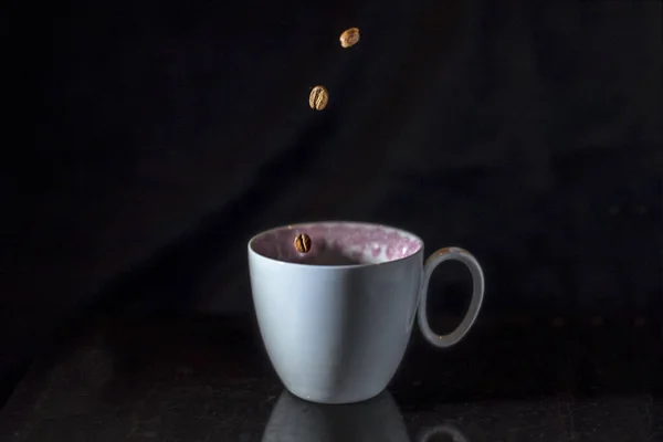 A white porcelain coffee cup with motion coffe beans on a black background, close up, isolated