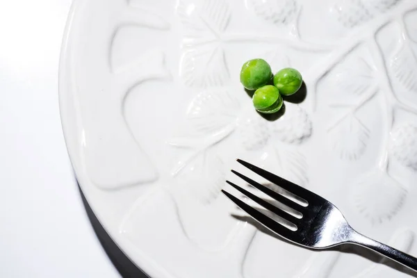 Three green peas on a white dining plate with a fork, close up, isolated