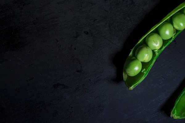 Fresh peas in a pea pod on a wooden black  background, isolated, macro photography