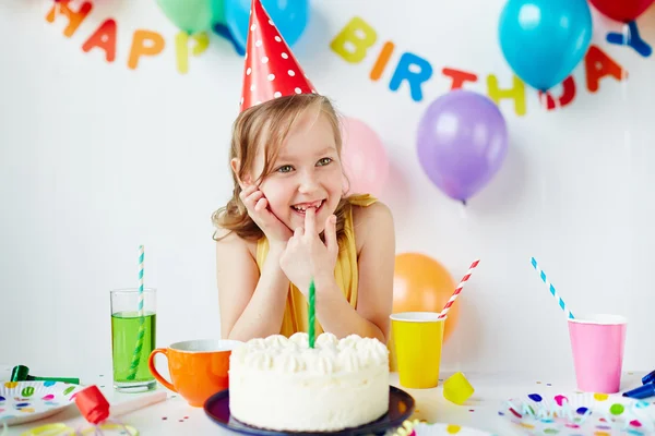 Menina em boné de aniversário sentado por bolo — Fotografia de Stock