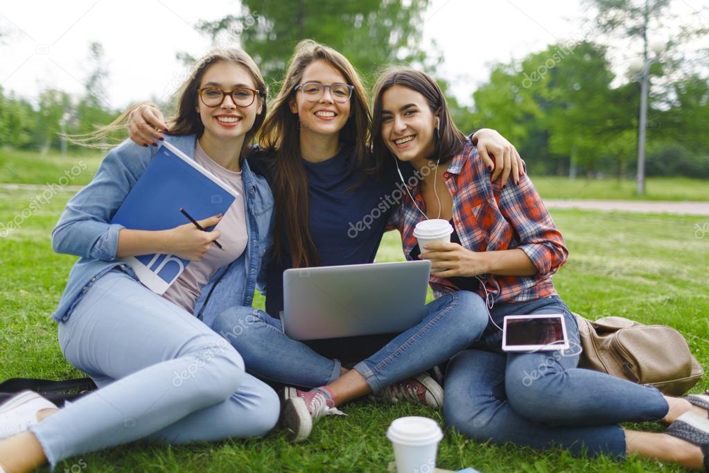 Happy students with gadgets sitting on lawn 