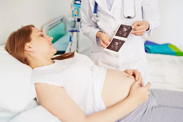 Беременная женщина смотрит на ультразвуковые фотографии — стоковое фото
