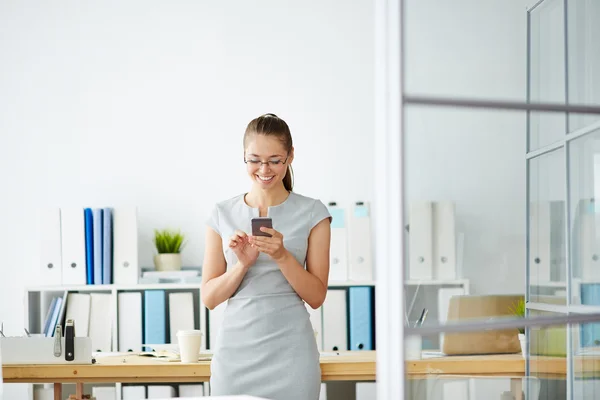 Молодая женщина, стоящая в офисе с телефоном — стоковое фото