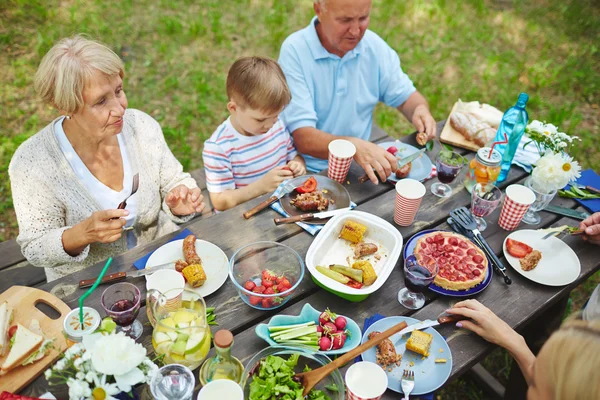 Семья сидит и ест мясо с овощами — стоковое фото