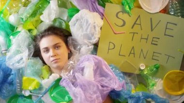 Yukarıdaki kavramsal yakın planda plastik torbalar ve şişelerle kaplı kızın geri dönüşüme başlaması için Save The Planet tabelasının yanına uzanması.