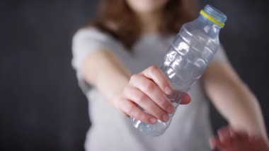 Seçici odak noktasında plastik su şişesinin orta kısmı kapanıyor ve genç kadın aktivist temiz çevre için onu buruşturuyor.