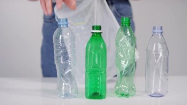 Beyaz arka plandaki ekolojiyi önemseyen genç kadın aktivistin çöp poşetine doldurduğu boş plastik şişelerin yakın çekim görüntüleri.
