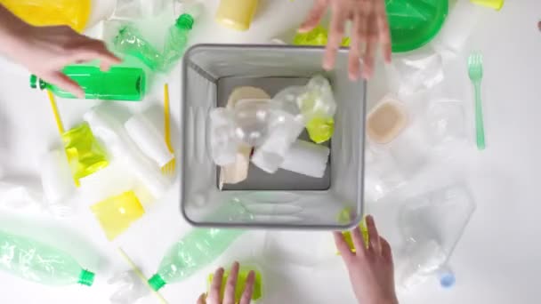 プラスチック製のアイテムを手に取り 白い背景のゴミ箱にそれらをドロップするのトップビューフラットレイ映像 — ストック動画