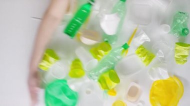 Yukardan gelen kavramsal, beyaz yüzeyden plastik parçaları ezen kırpık el görüntüsü.