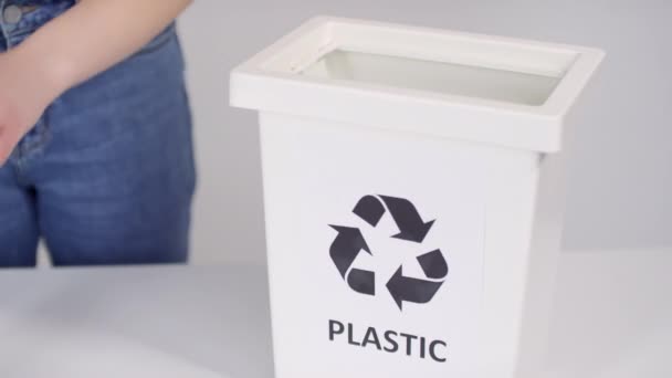 選択的焦点と認識できない手でプラスチック製のボトルを白い背景に入れて分別プラスチックをリサイクルするための容器 — ストック動画