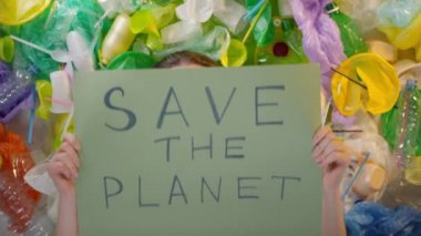 Kız astımlı bir kızın hava maskesi takıp uçan plastik bardaklardan korunması için Planet 'i Kurtarın tabelasını gösteren bir poster sergilendiği orta ölçekli bir fotoğraf.