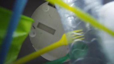 Plastik su şişelerini, çubukları ve fincanları plastik kirlilikten temizleyen, düşük açılı bir el fotoğrafı.