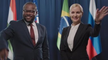 Afro-Amerikan politikacı ve bayan meslektaşının bayraklara karşı duran ve seyircilere el sallayan orta boy portresi