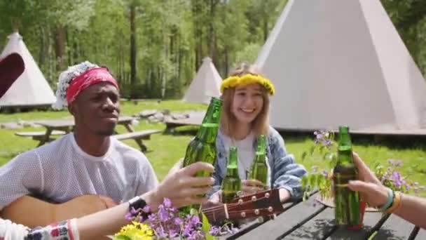 キャンプ場で小さなパーティーを開いた多民族の友人たちが 爽やかな飲み物で瓶を飲みながら笑顔で夏の時間を楽しんでいます — ストック動画