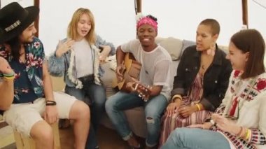 Afrika kökenli Amerikalı bir çocuk gitar çalarken en iyi arkadaşlarının yaz çadırında müzik eşliğinde dans edip şarkı söylediği yüksek açılı bir çekim.