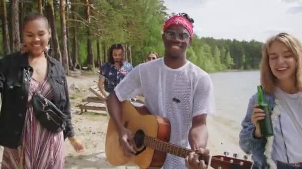 아프리카계 미국인젊은 음악가 기타를 연주하는 모습과 남자와 친구들이 호숫가를 음악에 — 비디오