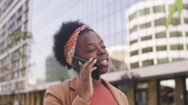  Modern iş merkezinin önünde dikilen ve cep telefonuyla konuşan neşeli Afro-Amerikan iş kadınının fotoğrafını çekiyorum.