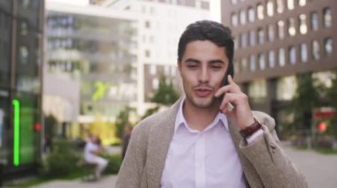  Dışarıda yürüyen ve cep telefonuyla konuşan mutlu ve yakışıklı işadamının yavaş izini sürüyorum.